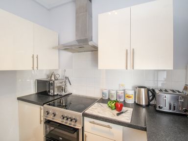 A kitchen with a stove oven microwave kettle toaster and vegetables on a cutting board at The Skipper's House in Weymouth