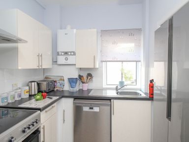 A kitchen with white cabinets stainless steel appliances a window above the sink and utensils in a container at The Skipper's House in Weymouth