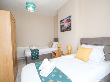 A bedroom with two beds a wooden wardrobe bedside tables lamps and a landscape picture on the wall at The Skippers House in Weymouth