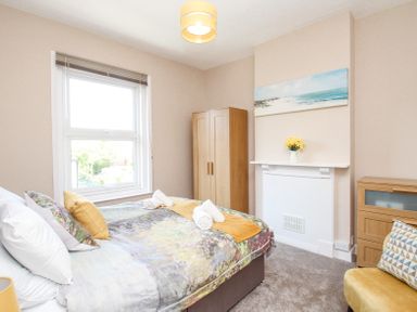A bedroom with a bed, wooden wardrobe, chair, cabinet, and a window at The Skipper's House in Weymouth