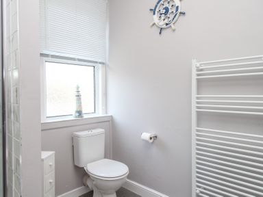 A bathroom with a toilet a window with blinds a lighthouse decoration a towel radiator and a nautical wheel wall decoration at The Skipper's House in Weymouth