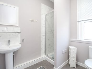 A bathroom with a pedestal sink a shower with glass door a small white drawer unit and a toilet at The Skippers House in Weymouth