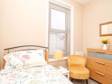 A bedroom with a bed a nightstand with a lamp a yellow chair a wooden dresser with a mirror and flowers at The Skipper's House in Weymouth
