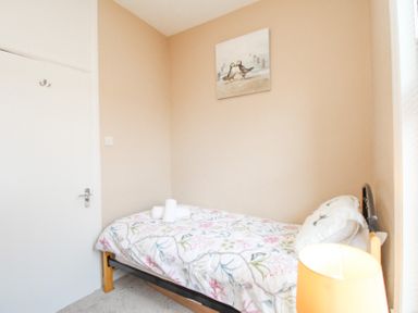 A small bedroom with a single bed and floral bedding a lamp and a painting on the wall at The Skipper's House in Weymouth