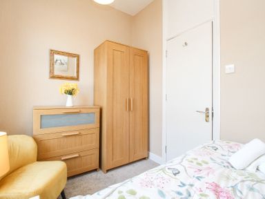 A bedroom with a wooden wardrobe a chest of drawers with flowers a yellow chair and a bed with floral bedding at The Skipper's House in Weymouth