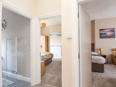 A hallway showing two bedrooms with beds, wardrobes, and bedside tables at The Skipper's House in Weymouth
