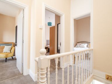 A hallway with three open doors showing a yellow chair and two bedrooms at The Skipper's House in Weymouth