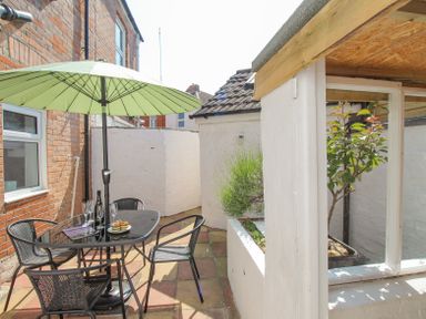 An outdoor patio area with a black metal table and chairs under a green umbrella at The Skipper's House in Weymouth