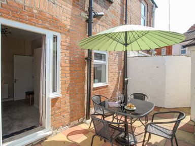 An outdoor patio with a table umbrella four chairs and a plate with cupcakes at The Skipper's House in Weymouth