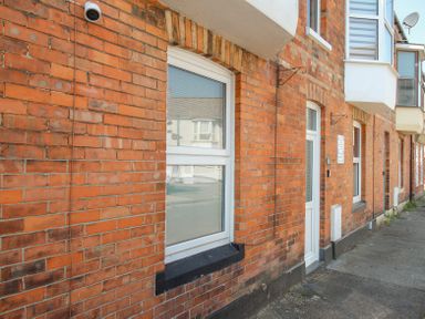 A red brick exterior wall with windows and doors along a sidewalk at The Skipper's House in Weymouth