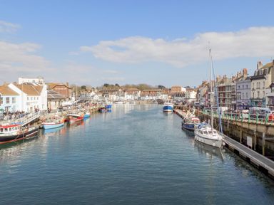A harbor with boats docked on both sides and buildings along the waterfront at The Skipper's House in Weymouth