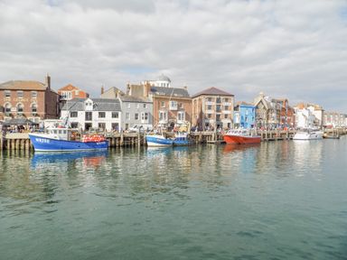 Boats docked along the harbor with buildings including a pub and cafes behind at The Skipper's House in Weymouth