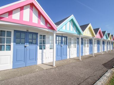 A row of beach huts with blue doors and multicolored gable roofs along a paved pathway at The Skipper's House in Weymouth