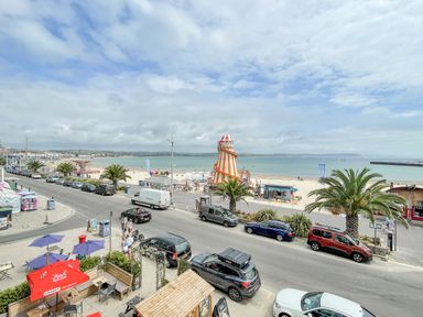 A street with parked cars and palm trees by a sandy beach with a helter skelter at The Skipper's House in Weymouth