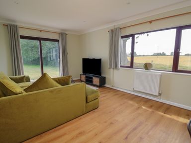 A living room with a green sofa a television on a stand and large windows overlooking fields at Sea View in St Clears