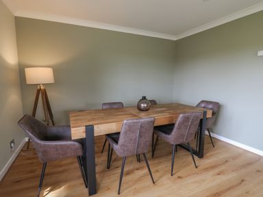 A dining room with a wooden table six chairs a floor lamp and a vase on the table at Sea View in St Clears