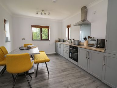 A kitchen with grey cabinets yellow chairs a table and windows at Sea View in St Clears