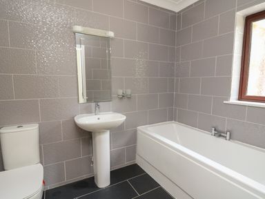 A bathroom with a toilet pedestal sink mirror bathtub and window at Sea View in St Clears