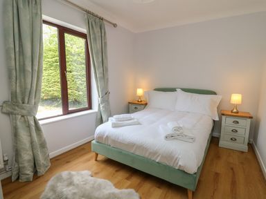 A bedroom with a bed with white linens two bedside tables with lamps curtains and a window showing green foliage at Sea View in St Clears