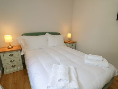 A bedroom with a double bed white bedding two bedside tables with lamps and folded towels at Sea View in St Clears