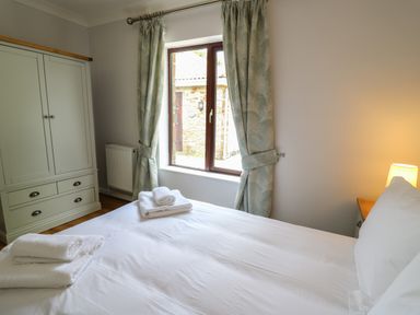 A bedroom with a bed with folded towels on it a wardrobe a window with curtains and a bedside lamp at Sea View in St Clears