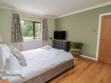 A bedroom with a bed towels on it a window with curtains a dresser with a TV and a green chair at Sea View in St Clears