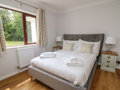 A bedroom with a double bed two bedside tables with lamps and a window with curtains at Sea View in St Clears