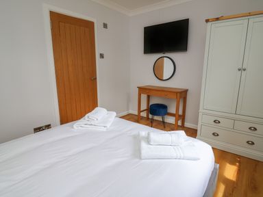 A bedroom with a wooden door a white wardrobe a wooden dressing table with a blue stool a wall-mounted television and a bed with white towels at Sea View in St Clears