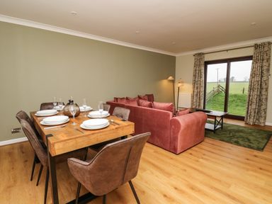 A dining table set with plates and glasses next to a pink sofa and a coffee table in a room with sliding glass door at The Oaks in St Clears