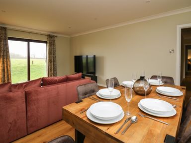 A dining table set with plates glasses and cutlery next to a living room with a red sofa and television at The Oaks in St Clears
