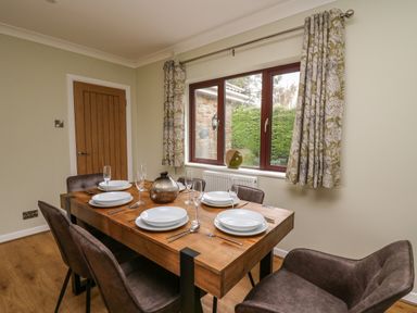 A dining room with wooden table set for six next to a window with patterned curtains at The Oaks in St Clears