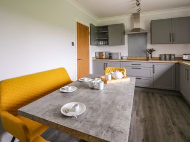 A kitchen with grey cabinets a wooden countertop a grey table set with white cups and plates and a yellow bench and chair at The Oaks in St Clears
