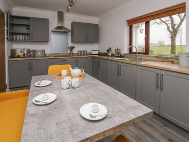 A kitchen with grey cabinets wooden countertops a gas stove a large window yellow chairs and a table with cups and plates at The Oaks in St Clears