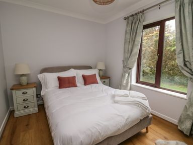 A bedroom with a double bed white bedding two red pillows two bedside tables with lamps and a window with curtains at The Oaks in St Clears