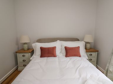 A bedroom with a double bed with white bedding and two brown cushions and two bedside tables with lamps at The Oaks in St Clears