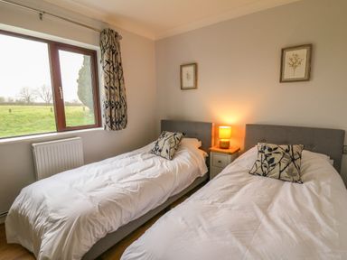 A bedroom with two single beds pillows lamp and framed pictures at The Oaks in St Clears