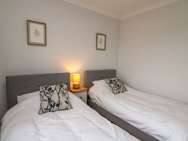 A bedroom with two single beds a bedside table with a lamp and framed pictures on the wall at The Oaks in St Clears