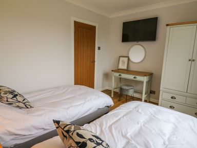 A bedroom with two beds a wooden door a wall mounted television a vanity table with a round mirror and a wardrobe at The Oaks in St Clears