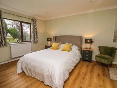 A bedroom with a bed two bedside tables lamps an armchair and a window at The Oaks in St Clears