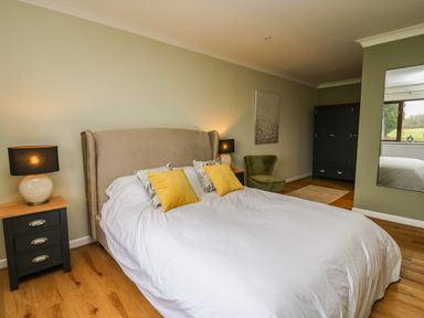 A bedroom with a large bed with yellow and patterned pillows bedside tables with lamps a green chair and a black wardrobe at The Oaks in St Clears