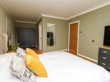 A bedroom with a bed with yellow and patterned pillows a black wardrobe a wooden door a wall mirror and a dresser with a TV at The Oaks in St Clears