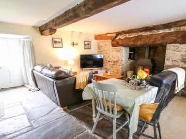 A living room with a brown leather sofa a dining table with two chairs a wood burning stove and a television at The Bake House in Bettws