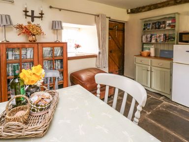 A kitchen area with a wooden cabinet filled with DVDs a basket on a table with a wine bottle and cookies a wooden door and a green cupboard with brochures and a microwave at The Bake House in Bettws