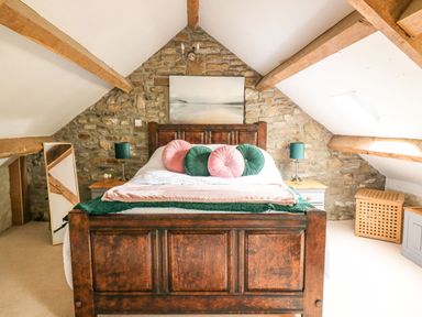 A bedroom with a wooden bed frame stone wall exposed wooden ceiling beams and bedside tables at The Bake House in Bettws