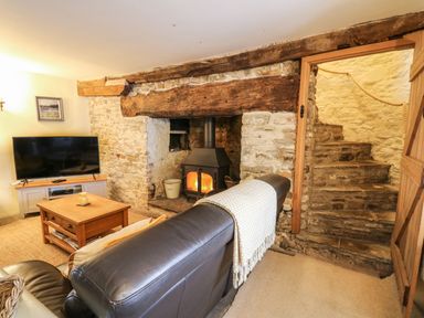 A living room with a stone fireplace wood stove leather sofa wooden coffee table television and stone staircase at The Bake House in Bettws