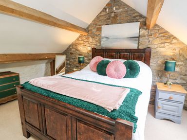 A bedroom with a wooden bed frame pillows and bedside tables under slanted ceilings at The Bake House in Bettws