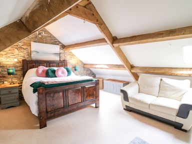 A bedroom with a wooden bed frame pillows two bedside tables lamps a white sofa and exposed wooden beams at The Bake House in Bettws