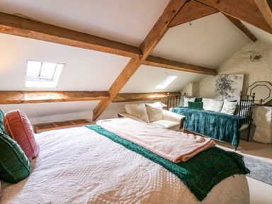A bedroom with a bed a white sofa and a daybed under wooden beams at The Bake House in Bettws