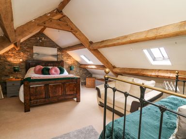 A bedroom with wooden beams stone wall a wooden bed and a white sofa at The Bake House in Bettws
