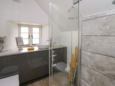 A bathroom with a glass shower, sink on a countertop, yellow towels, and a small window at The Bake House in Bettws